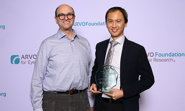 Two men stand next two each other against a lavender backdrop with the words &ldquo;ARVO Foundation.&rdquo; 