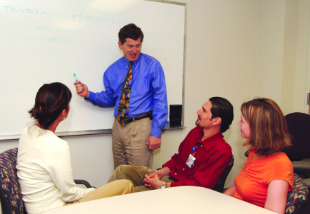 Mark Servis, in a photo taken years ago, stands in front of whiteboard while addressing medical students sitting in chairs. 