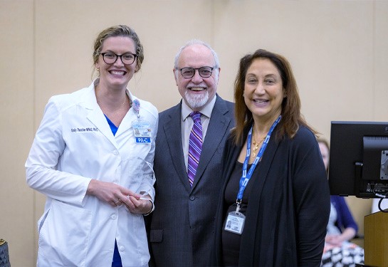 Clinician in white coat, left, holds crystal award standing next to two faculty leaders