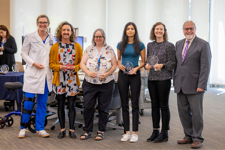 Dean Stephen Cavanagh, right, stands next to six award winners, each holding a crystal award