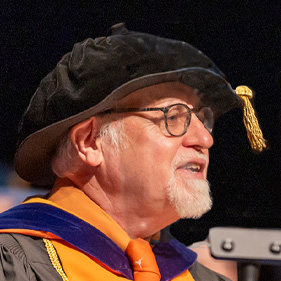 Nursing dean wearing hat with tassel speaks to crowd from podium