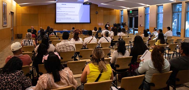 A group of people seated in chairs in the MIND Institute auditorium listen to a speaker giving a presentation