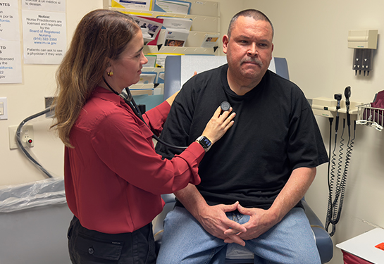 A doctor listens to her patient’s heartbeat with a stethoscope during a checkup in a medical exam room.