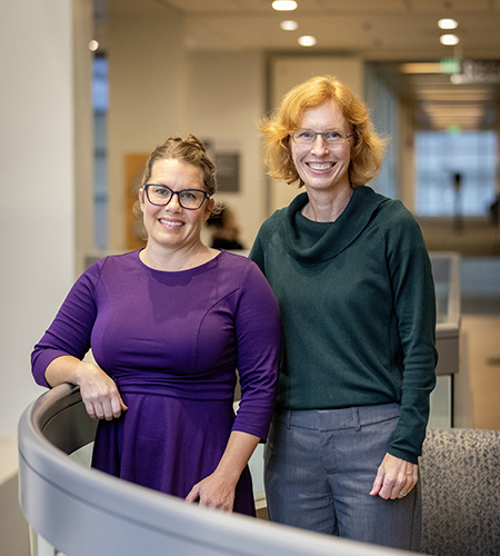 Two women standing next to each other at railing.
