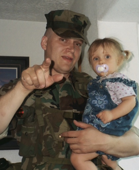 A U.S. Marine corporal in uniform holds his young daughter as they pose together.