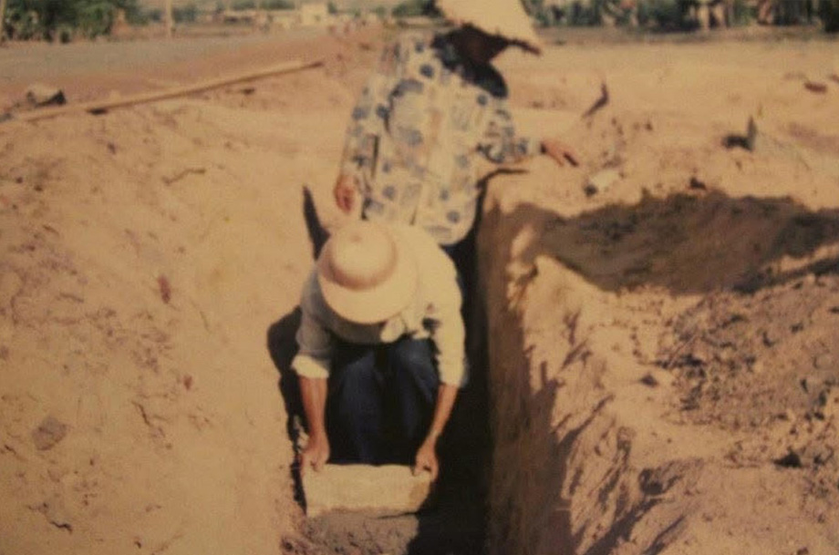 Historical photo of two men digging dirt trench in Vietnam to build a house