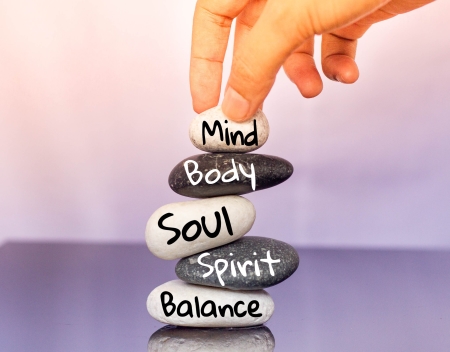 A hand hovers above stack of rocks with the painted words: mind, body, soul, spirit and balance.