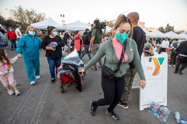 A woman wearing a mask pulls a cart loaded with supplies.