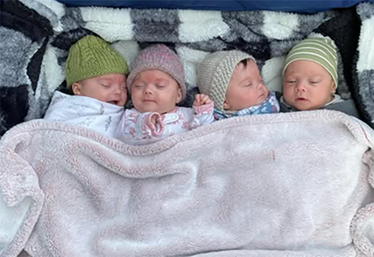 Four babies lying together on a blanket with matching outfits on.